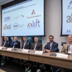 Six men sit at a long table. On the wall behind them are screens displaying institute logos.
